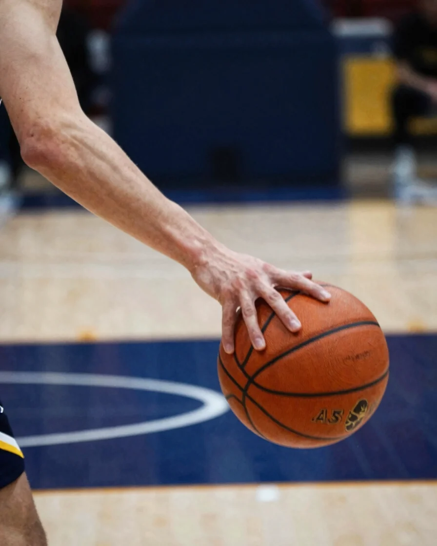 Close-up of a basketball player's hand dribbling the ball on a polished court, motion blur on the ball, sharp focus on t